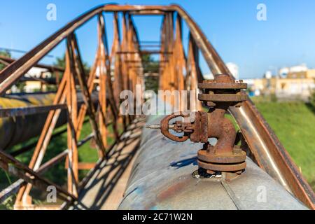 Alte rostige Eisenbrücke über den Fluss mit Dampfleitung. Wärmeversorgung. Industrieanlagen. Detailansicht eines Dampfrohrleitungsventils. Stockfoto