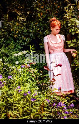 Junge Frau im Dirndl in Ihrem Garten und hält eine gelbe Rose in der Hand. Stockfoto