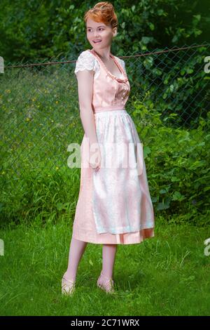 Junges Mädchen mit rot-blonden Haaren, auf einer Wiese im Dirndl stehend. Stockfoto