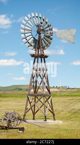 Vintage Windmühle vor einem blauen Himmel auf ländlichen Ackerland in diesem vertikalen Bild von Retro-Bauernhof Ausrüstung und Maschinen. Stockfoto