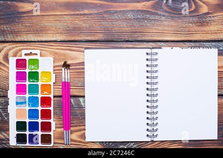 Notizbuch, Farben und Pinsel auf einem Holztisch, Draufsicht Stockfoto