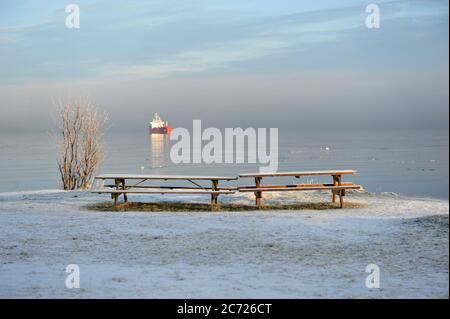 Schiff Offshore an frostigen Wintertag. Bänke am Strand im Vordergrund. Horizontales Foto mit Kopierbereich. Stockfoto