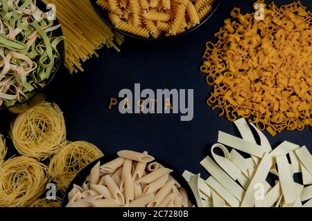 Rohe runde Pasta auf dunklem Hintergrund. Das Wort PASTA aus Holzbuchstaben in der Mitte. Das Konzept der köstlichen Speisen. Draufsicht, flaches Layout, Kopie Stockfoto