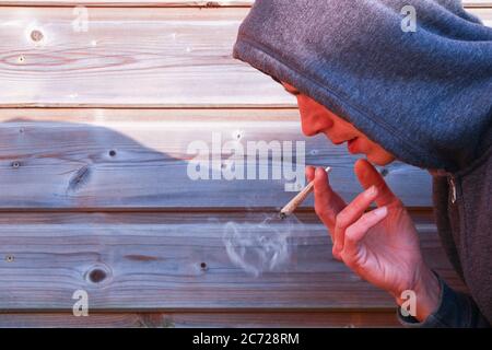 Junge mit einem gerollten Zigaretten mit einem faltige Hand. Mann Rauchen von Marihuana gegen einen hölzernen Lattenzaun Stockfoto