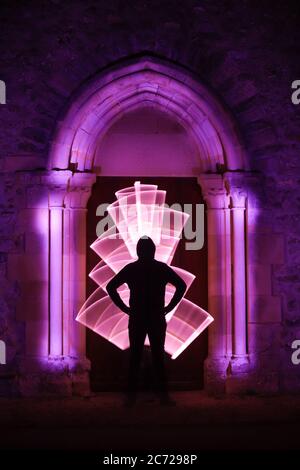 Lightenpainting-Session an einem mystischen Ort. Kreisform mit einem leichten Säbel. Silhouette eines Mannes mit einer Lichtkurve hinter ihm. Architektur Gothic. Stockfoto