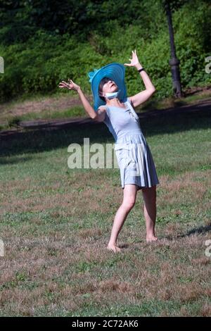 Eine asiatisch-amerikanische Frau mit ihrer Maske um den Hals tanzt in einem offenen Feld in Flushing, Queens, New York City. Stockfoto