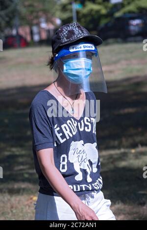 Eine schlanke asiatische amerikanische Frau für einen Übungsspaziergang trägt sowohl eine chirurgische Maske und ein Gesichtsschild. In Flushing, Queens, New York City. Stockfoto