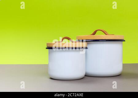 Zwei neue Metallkasserolle mit Holzdeckel auf einem grauen Tisch und grünem Hintergrund. Platz für Text Stockfoto