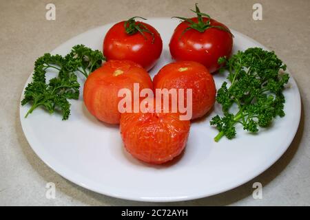 Vegane Küche. Vegetarische Gerichte. Platte von Rohheit. Tomaten frisch rot und geschält nach dem Kochen. Zweige der grünen Petersilie. Stockfoto