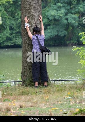 BAUM UMARMT. Ein asiatischer Amerikaner scheint einen Baum in der Nähe des Sees im Kissena Park, Flushing, New York City, zu umarmen. Stockfoto