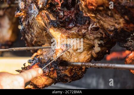 Portionierung von gebratenem Schwein, Schneiden von Fleisch.. Schwein gegrillt traditionelle Kohle und Feuer. Das kleine Schwein wird auf einem offenen Feuer ganz geröstet. Schwein auf dem Spieß. Stockfoto