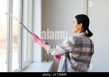 Junge Frau in Handschuhen putzt das Fenster mit Mopp im Büro Stockfoto