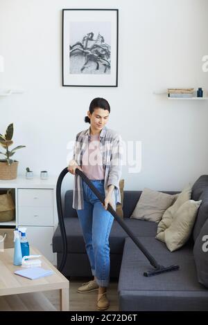 Junge Magd mit Staubsauger im Wohnzimmer sie saugen Staub vom Sofa Stockfoto