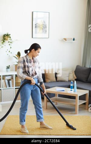 Junge Frau mit Staubsauger, um den Teppich im Wohnzimmer zu saugen Stockfoto