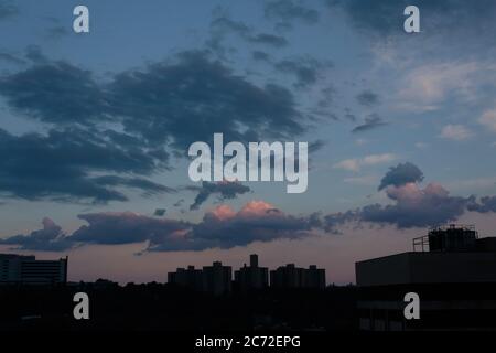 Ein blauer, wolkiger Himmel in der Abenddämmerung mit warmen orange und violetten Untertönen über der Bronx Skyline Stockfoto