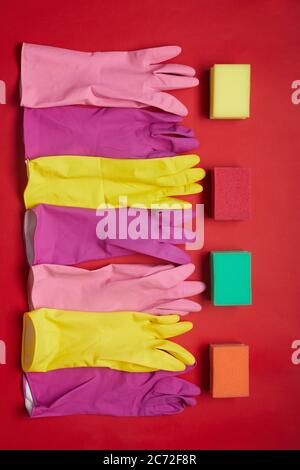 Hohe Winkelansicht von Gummihandschuhen und Schwämmen, die in einer Reihe isoliert auf rotem Hintergrund liegen Stockfoto