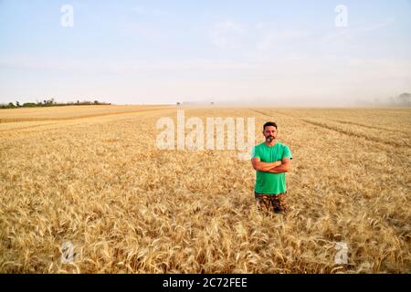 Glücklicher Bauer stolz im Weizenfeld mit gekreuzten Armen auf der Brust. Agronom trägt Corporate Uniform, Blick auf die Kamera auf Ackerland. Reich Stockfoto