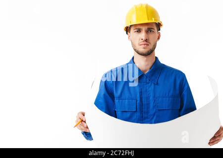Junge ernsthafte Vorarbeiter in blauen Uniform und gelben Helm nachdenklich Blick in Kamera halten Plan des neuen Projekts in den Händen über weißem Hintergrund Stockfoto
