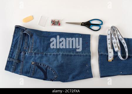 Gerade geschnittene blaue denip Shorts, Maßband, Schere und Nähnadel auf einem weißen Tisch. Kürzen Sie die Jeans mit einer Schere und einer Nähnadel. DIY. Stockfoto