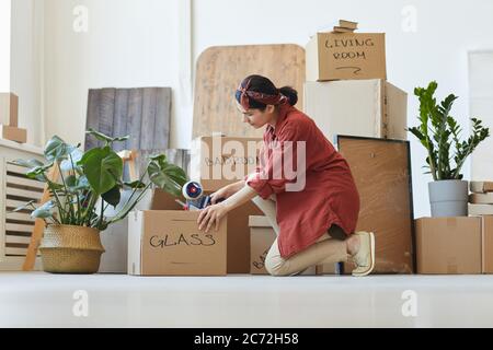 Junge Frau versiegelt die Boxen mit Dingen mit Klebeband während der Verlegung Stockfoto