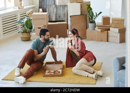 Junges Paar auf dem Teppich sitzen und Pizza essen sie ruhen nach Umzug Stockfoto