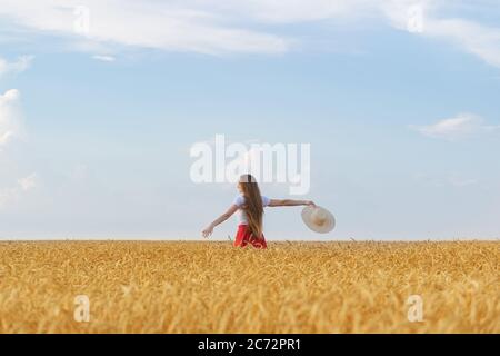 Junge Frau geht durch Weizenfeld mit Hut in den Händen und genießen sonnigen Tag. Freiheit und Ruhe. Stockfoto