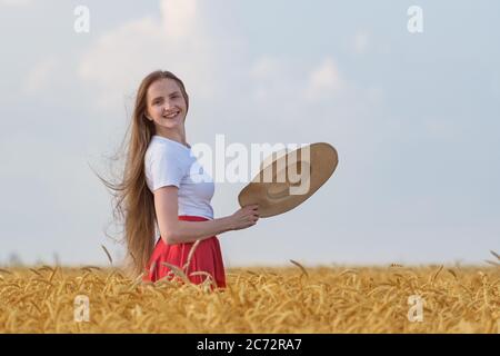 Junge Frau mit braunen Haaren steht im Feld von reifen Weizen hält Hut. Urlaub auf dem Land. Stockfoto