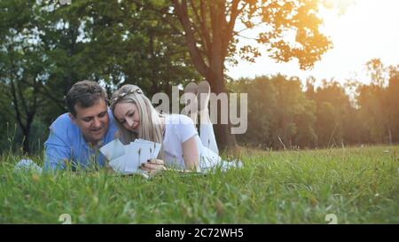 Ein Mann und ein Mädchen schauen sich ein Familienalbum mit Fotos im Park auf dem Rasen an. Stockfoto