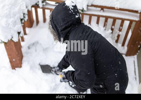 Rückansicht der Person in der Winterkleidung Biegen beim Schaufeln Schnee mit einer Schaufel, Schneeräumung durch einzelne aus dem Haus Hinterhof nach Schneefall. Stockfoto