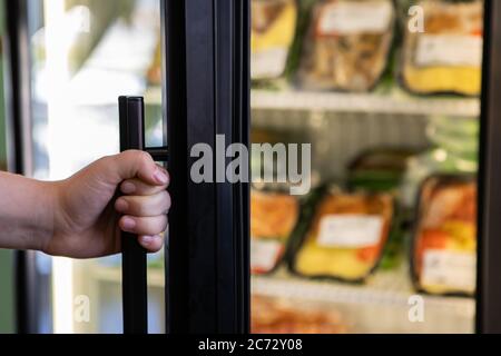 Selektive Fokussierung und Nahaufnahme der Hand, die den Griff des Kühlschranks im Supermarkt hält, verschwommene Lebensmittel im Hintergrund. Mit Kopierplatz. Stockfoto