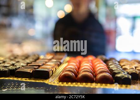 Vielfalt an köstlichen Schokolade Süßigkeiten Trüffel Desserts auf einer Patisserie Display Kühlschrank in selektiver Fokus-Ansicht mit verschwommener Person im Hintergrund Stockfoto