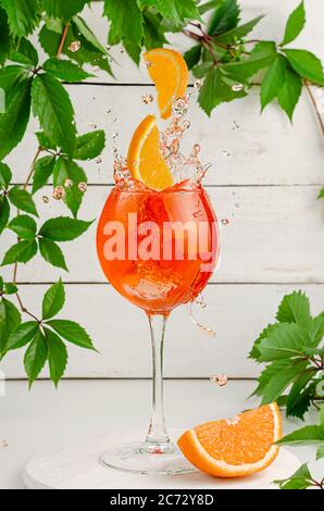 Orangenscheiben fallen in spritzendem aperol-Cocktail. Erfrischender italienischer Sommerdrink auf weißem Holzhintergrund. Stockfoto