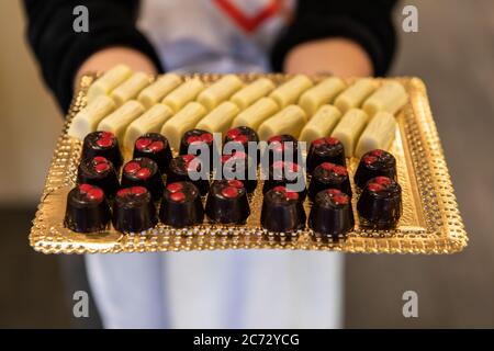 Selektive Fokus auf zwei Arten von köstlichen Schokolade Desserts auf goldenem Tablett von Frau in verschwommenem Hintergrund gehalten. Empfang Buffet Süßigkeiten und Bonbons. Stockfoto