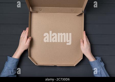 Leere offene Schachtel Pizza in Kinderhände. Schwarzer Hintergrund. Draufsicht. Speicherplatz kopieren Stockfoto