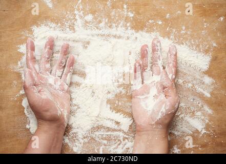 Zwei Hände und Weizenmehl auf einem braunen Holzhintergrund verstreut, Produkt ist über die Oberfläche verteilt, Küche Hintergrund, Draufsicht Stockfoto