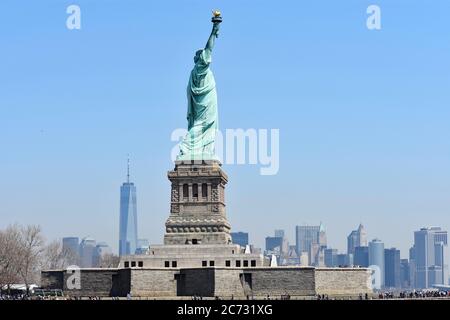 Ein Seitenblick auf die Freiheitsstatue auf Liberty Island, Manhattan. Die Skyline von Downtown New York ist hinter der Statue sichtbar. Stockfoto