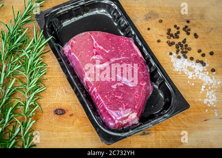 Rindersteak in vakuumverpackter Haut und Gewürze auf Holzhackbrett Stockfoto