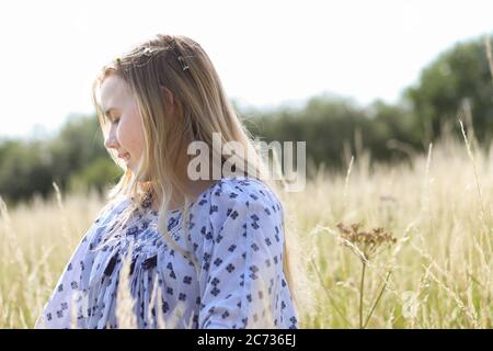 Ein junges hübsches Hippie-Mädchen mit blonden Haaren im Sonnenschein auf einem Weidefeld im Sommer. Stockfoto