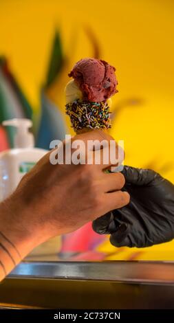 Verkäufer in Schürze hält Eis in einem Waffelkegel, Nahaufnahme. Verkauf von Eis in einem Geschäft Stockfoto