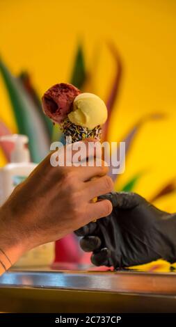 Verkäufer in Schürze hält Eis in einem Waffelkegel, Nahaufnahme. Verkauf von Eis in einem Geschäft Stockfoto