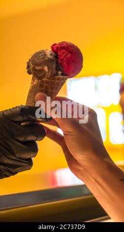 Verkäufer in Schürze hält Eis in einem Waffelkegel, Nahaufnahme. Verkauf von Eis in einem Geschäft Stockfoto