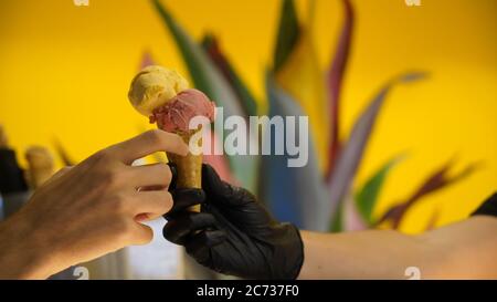 Verkäufer in Schürze hält Eis in einem Waffelkegel, Nahaufnahme. Verkauf von Eis in einem Geschäft Stockfoto