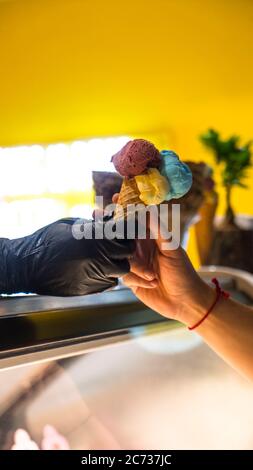 Verkäufer in Schürze hält Eis in einem Waffelkegel, Nahaufnahme. Verkauf von Eis in einem Geschäft Stockfoto