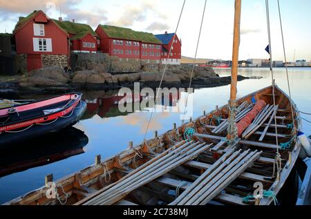 Ein traditionelles Färöer Ruderboot Docking in Torshavn Hafen mit Rasen überdacht Holzhäuser in Tinganes im Hintergrund.Torshavn.Streymoy.Färöer Inseln.Territorium von Dänemark Stockfoto