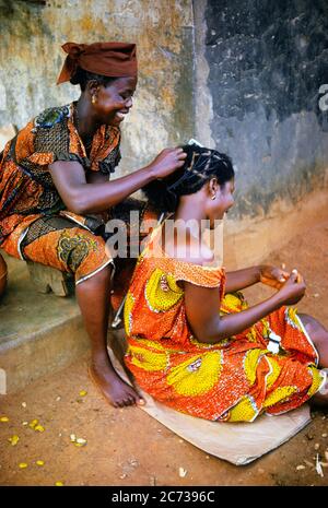 1970ER BÜRGERSTEIG BEAUTY SALON LÄCHELND FRAU FRISEUR FLECHTEN HAAR DES KUNDEN ODER FREUND IN EINEN TRADITIONELLEN STIL GHANA AFRIKA - KR23808 SPE001 HARS KARRIERE JUNGE ERWACHSENE SALON BAUMWOLLE FREUDE LIFESTYLE FRAUEN JOBS LÄNDLICHEN AFRIKA HAUS LEBEN KOPIEREN RAUM FREUNDSCHAFT IN VOLLER LÄNGE HALBLÄNGE DAMEN PERSONEN TUCH TRADITIONELLEN BERUF GESCHWISTER SCHWESTERN FRAU BUNTE GESCHICKLICHKEIT BERUF GLÜCK FÄHIGKEITEN FRÖHLICH HIGH-ANGLE STILE KARRIERE SCHWARZ ETHNIZITÄT BERUFE GESCHWISTER LÄCHELT VERBINDUNG KONZEPTIONELLE FLECHTEN KULTUR FRÖHLICH STYLISH FRISEUR ZUSAMMENARBEIT MODE ZWEISAMKEIT JUNGE ERWACHSENE FRAU Stockfoto