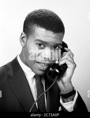 1950S 1960S SERIOUS SMILING AFROAMERIKANISCHEN MANN GESCHÄFTSMANN TRAGEN ANZUG UND KRAWATTE BLICK AUF KAMERA TELEFONGESPRÄCH - N248 HAR001 HARS FREUDE LIFESTYLE GESUNDHEIT HALBWERTSZEIT PERSONEN MÄNNER VERTRAUEN AUSDRÜCKE B & W BLICKKONTAKT ZIELE ERFOLG ANZUG UND KRAWATTE TRÄUME VERKAUFEN GLÜCK KOPF UND SCHULTERN FRÖHLICHER KUNDENSERVICE AFRO-AMERIKANER MUT AFRO-AMERIKANER UND WAHL WISSEN FÜHRUNG FORTSCHRITT ERHOLUNG SCHWARZ ETHNIZITÄT STOLZ IN AUF BERUFE POLITIK LÄCHELT VERBINDUNG KONZEPTIONELLE FREUDIG STILVOLLE ZUSAMMENARBEIT WACHSTUM VERKÄUFER TRAGEN JUNGEN ERWACHSENEN MANN SCHWARZ UND WEISS HAR001 Stockfoto