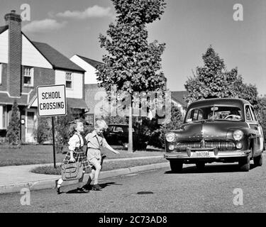 1940ER JAHRE ZWEI SCHULKINDER MÄDCHEN JUNGE ZUSAMMEN LAUFEN KREUZUNG SUBURBANEN STRASSENECKE VOR DER ANNÄHERUNG KOMBI AUTO - S3977 HAR001 HARS TEAMWORK LIFESTYLE GESCHWINDIGKEIT FRAUEN BRÜDER ZU HAUSE LEBEN KOPIEREN RAUM FREUNDSCHAFT VOLLE LÄNGE AUTO PFLEGE GEFAHR MÄNNER RISIKO ECKE GESCHWISTER SCHWESTERN TRANSPORT S&W SCHULEN WEITWINKEL GRAD ABENTEUER GEFÄHRLICH SCHUTZ STÄRKE UND AUTOS AUSSEN NIEDRIGEN WINKEL LEISTUNGSFÄHIGE RICHTUNG IN DER PRIMÄREN GESCHWISTER POTENZIAL KONZEPTUELLE AUTOMOBILE FAHRZEUGE VORSICHT KLASSE SCHULWACHSTUM JUGENDLICHE GESTOPPT ZWEISAMKEIT AHNUNGSLOS NÄHERT SICH SCHWARZ UND WEISS Stockfoto