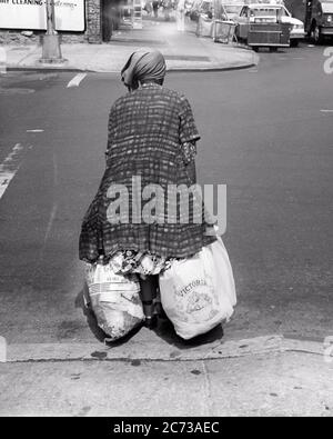 80S AFRICAN-AMERICAN BAG LADY CROSSING STREET BACK VIEW TRAGEN ZERLUMPTER KLEIDUNG TRAGEN VON PLASTIKTÜTEN MIT HABSELIGKEITEN GEFÜLLT - V287 HAR001 HARS LIFESTYLE FRAUEN MOODY ARMEN AUSGESTOPFTEN HÄUSLICHEN LEBENS VEREINIGTE STAATEN KOPIEREN RAUM IN VOLLER LÄNGE DAMEN PERSONEN VEREINIGTE STAATEN VON AMERIKA RISIKO NERVÖS BEUNRUHIGT B & W BETROFFEN TRAURIGKEIT ANGST HOCHWINKEL OBDACHLOS WOHLFAHRT AFRO-AMERIKANER AFROAMERIKANER BRACH VERZWEIFLUNG SCHWARZE ETHNIZITÄT RÜCKANSICHT STIMMUNG NYC PSYCHISCHE GESUNDHEIT KONZEPTIONELL VON HINTEN GLUM NEW YORK STÄDTE MITTELLOS ZERRISSEN NEW YORK STADT ANONYME SPANNUNG RÜCKANSICHT MITTELLOS MISERABLE HABSELIGKEITEN SCHWARZ UND WEISS Stockfoto