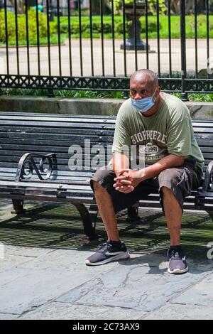 New Orleans, Louisiana/USA - 8. 7. 2020: Mann mit Gesichtsmaske und sitzt auf einer Parkbank am Rande des Jackson Square im French Quarter Stockfoto