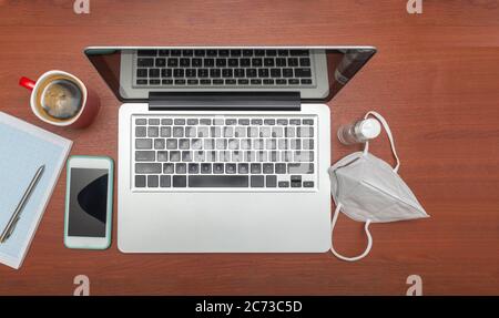 Computer mit Maske und Desinfektionsmittel-Gel an einem Arbeitsplatz neben Notebook, Handy und Kaffeetasse Stockfoto